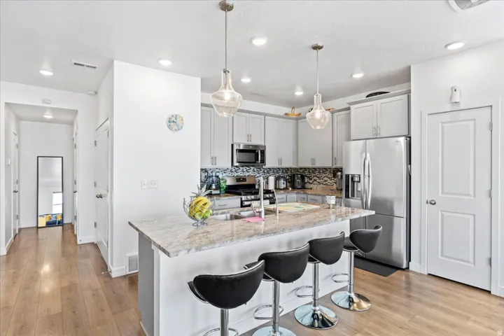 Kitchen featuring a large island with stone countertop, stainless steel appliances, pendant lighting, and wood-finish flooring