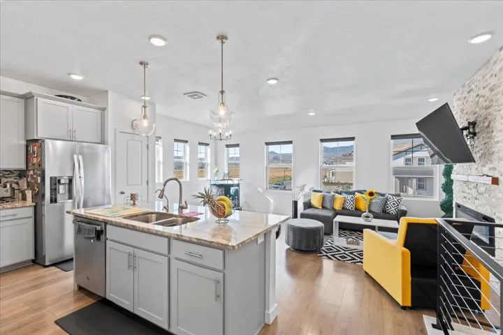 Open-concept living space featuring a kitchen island with stone countertop, stainless steel appliances, wood-finish flooring, and a fireplace with a stone surround