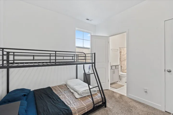Carpeted room with a window providing natural light, white walls, and a door leading to a bathroom