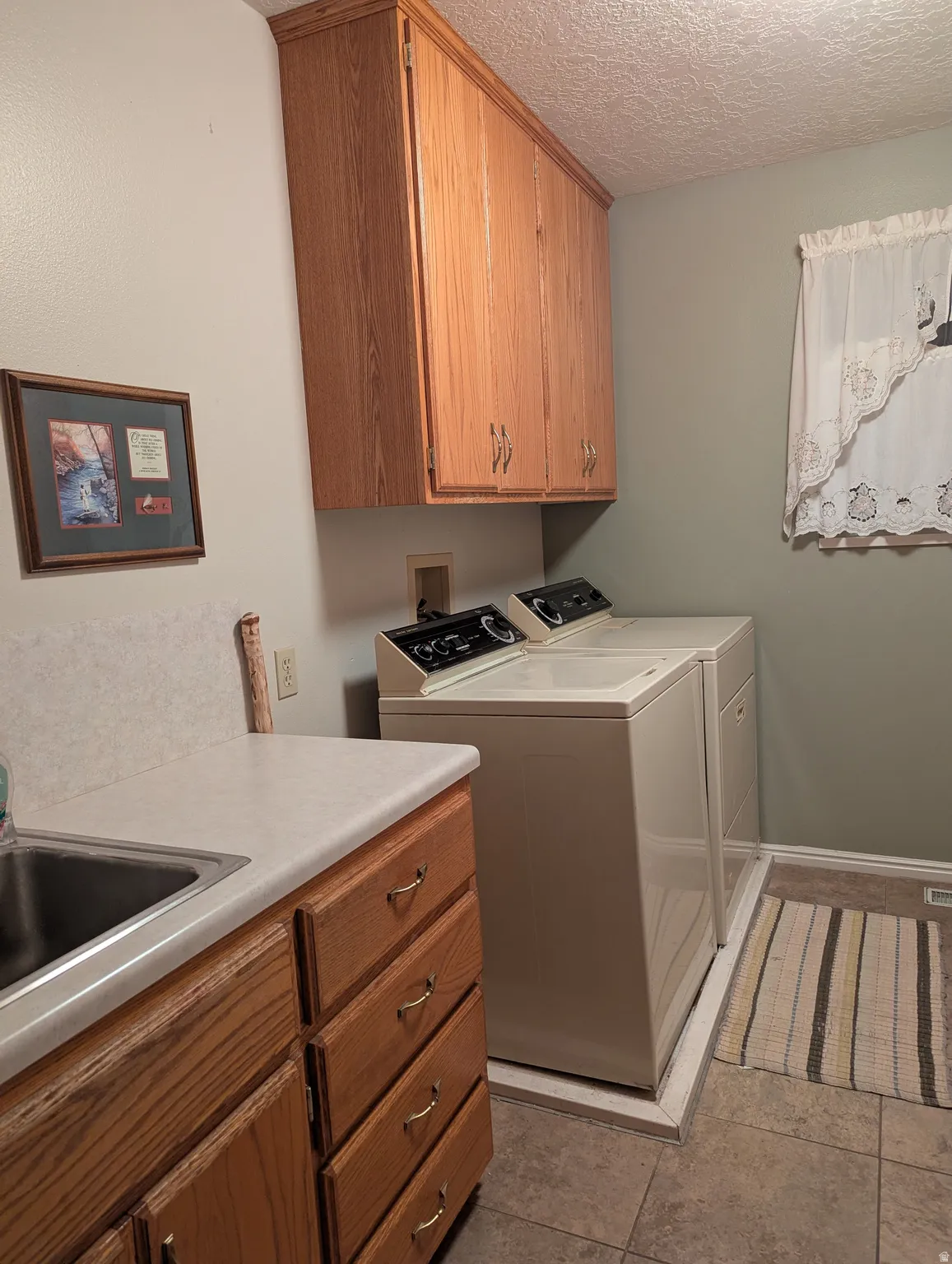Functional laundry space featuring wood-finish cabinetry, a utility sink with a laminate countertop, and tile flooring
