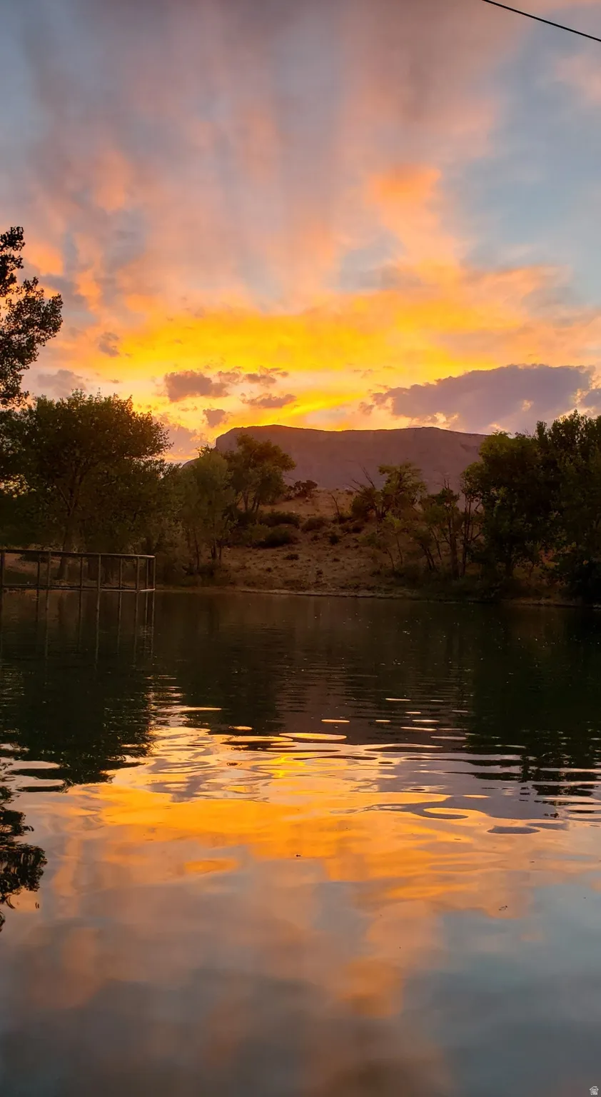 Natural body of water with surrounding foliage, reflected clouds, and distant mountain landscape