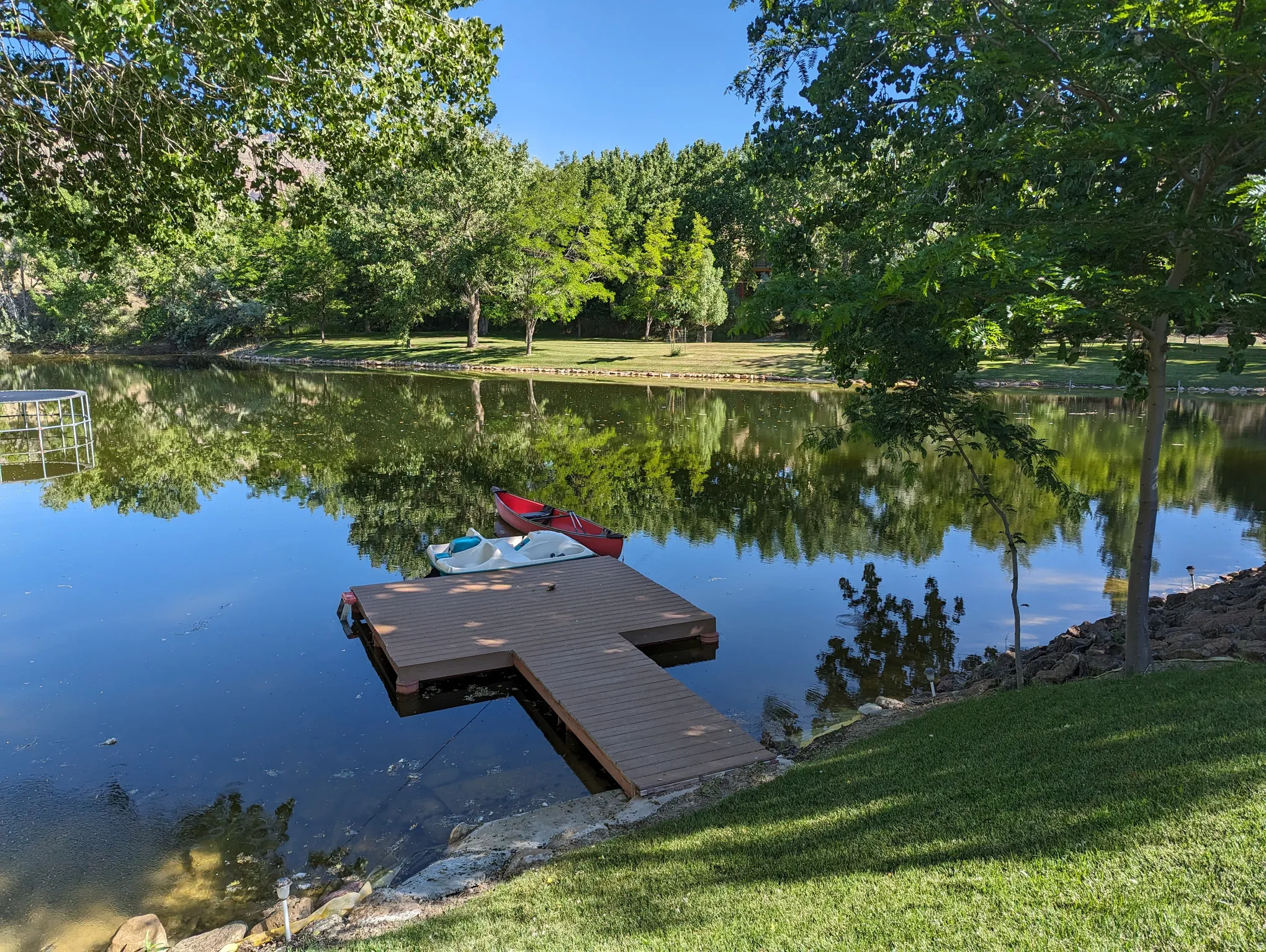 Manicured lawn leading to a private pond with a wood-finish dock
