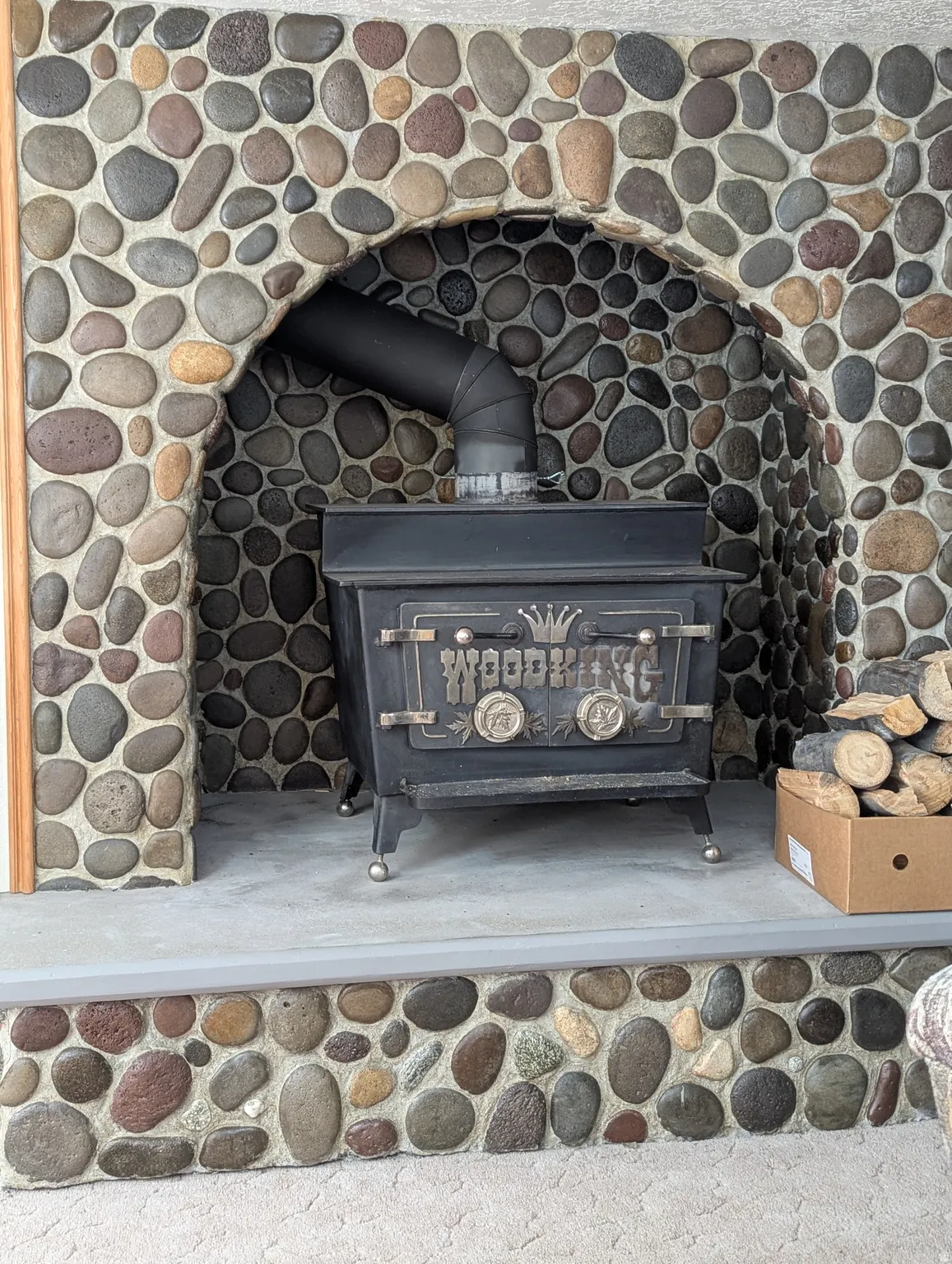 River rock fireplace surround with an arched opening, featuring a solid fuel burning stove