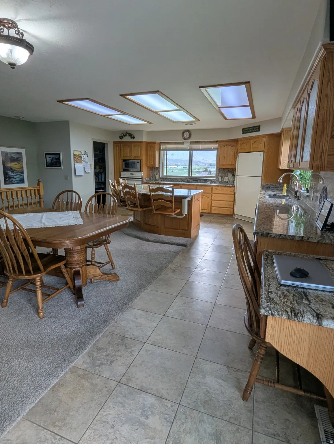 Spacious open-concept kitchen and dining area featuring wood cabinetry, stainless steel appliances, granite countertops, and tile flooring