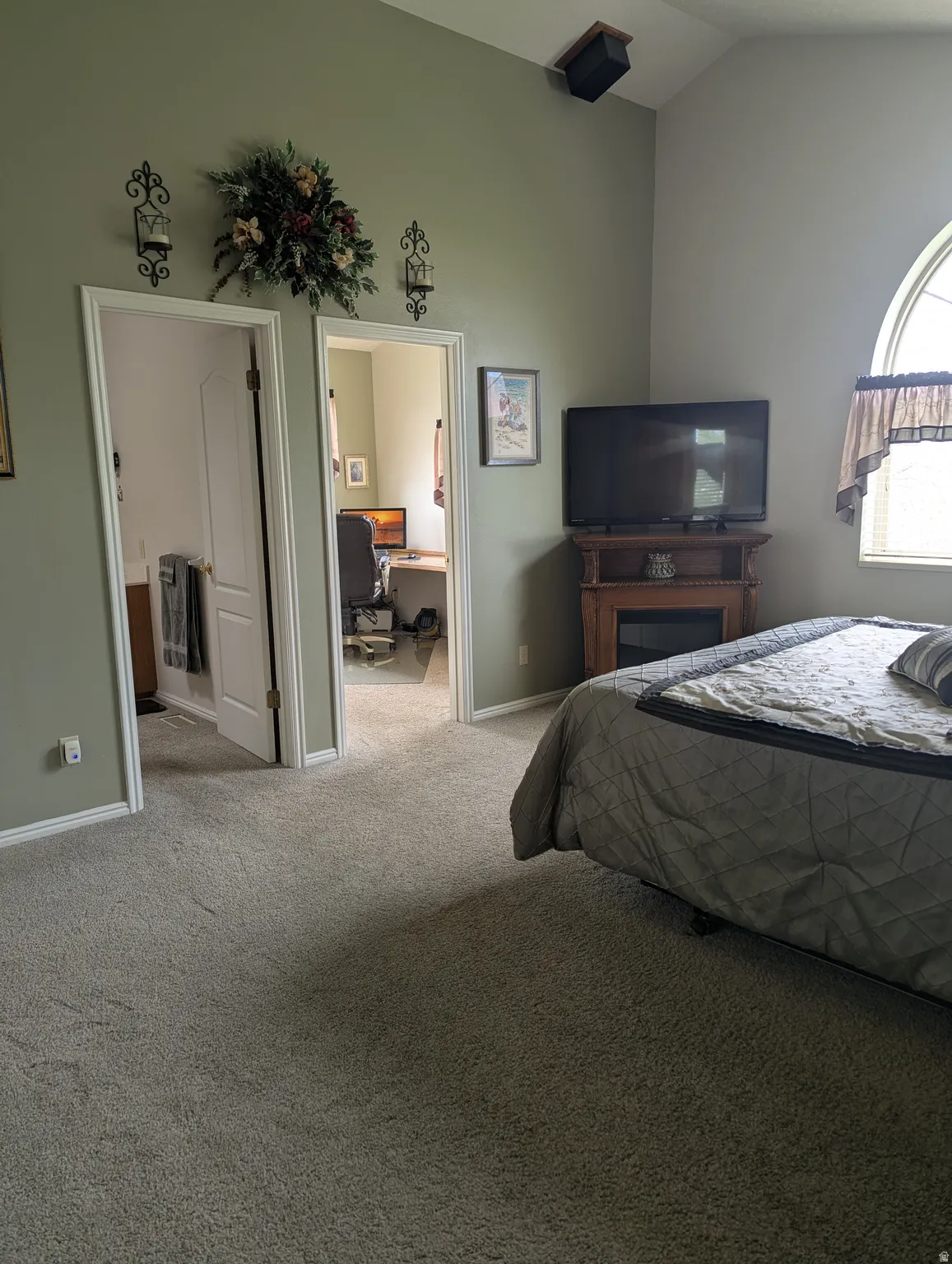Vaulted ceiling, arched window, built-in fireplace mantel, and soft carpet flooring