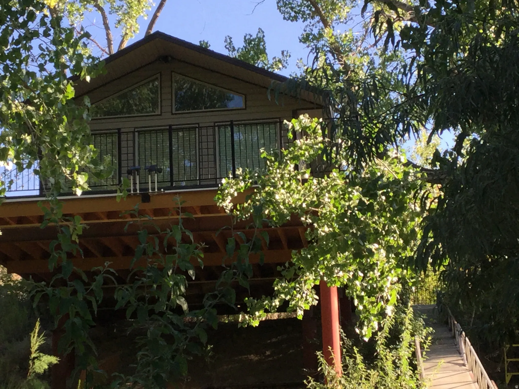 Elevated structure with a wood-finish exterior, upper-level deck with black railings, and multiple windows