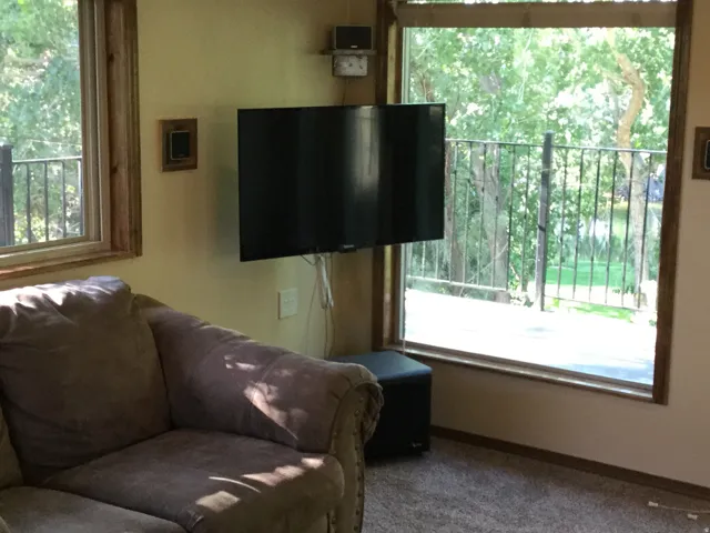 Expansive windows with natural wood trim, wall-mounted television, and neutral-toned wall paint