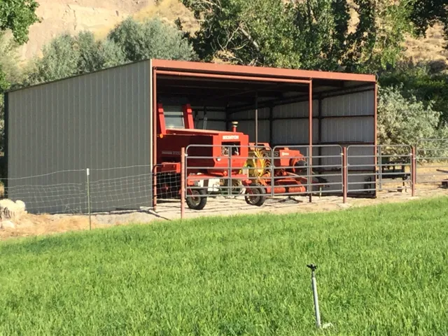 Metal-sided outbuilding with an open-air bay, corrugated metal roof, and durable metal fencing