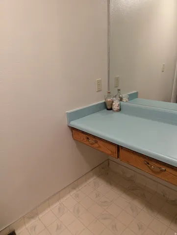 Floating vanity with integrated storage drawers, light blue countertop, and a large wall-mounted mirror