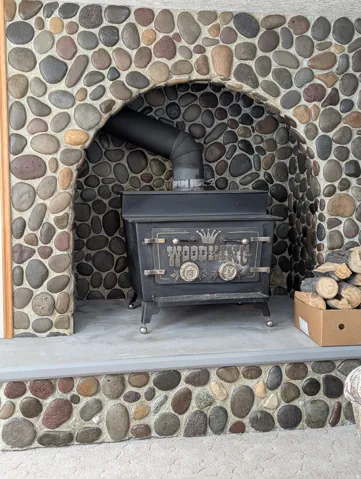 River rock fireplace surround with an arched opening, featuring a solid fuel burning stove