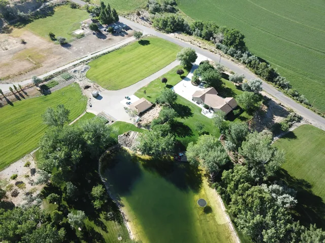 Expansive property featuring a large body of water, extensive green lawns, mature trees, a private driveway, and a residential structure with a shingled roof