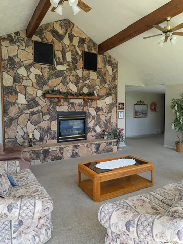 Vaulted ceiling with exposed wood beams, stone-faced fireplace with hearth, built-in fireplace insert, and ceiling fans