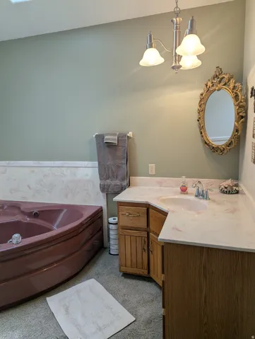 Corner soaking tub, dual-tone vanity with integrated sink, stone-finish countertop, and brushed nickel light fixture