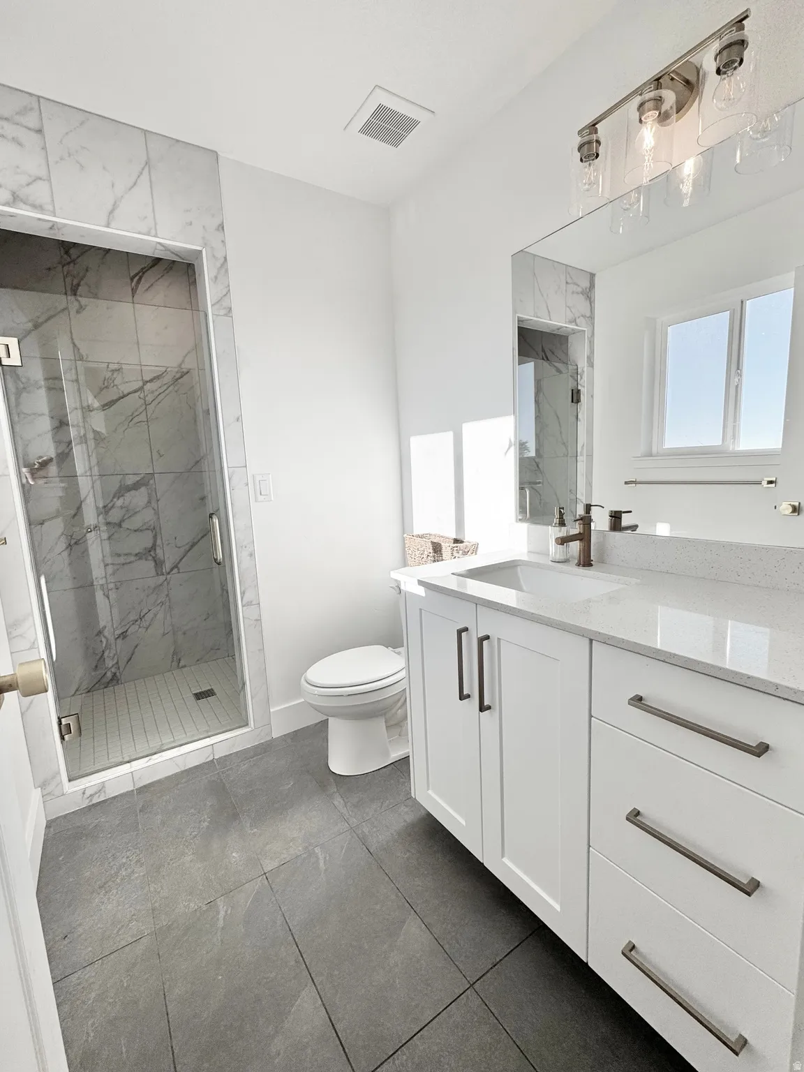 Walk-in shower with clear glass enclosure and marble-style tile surround