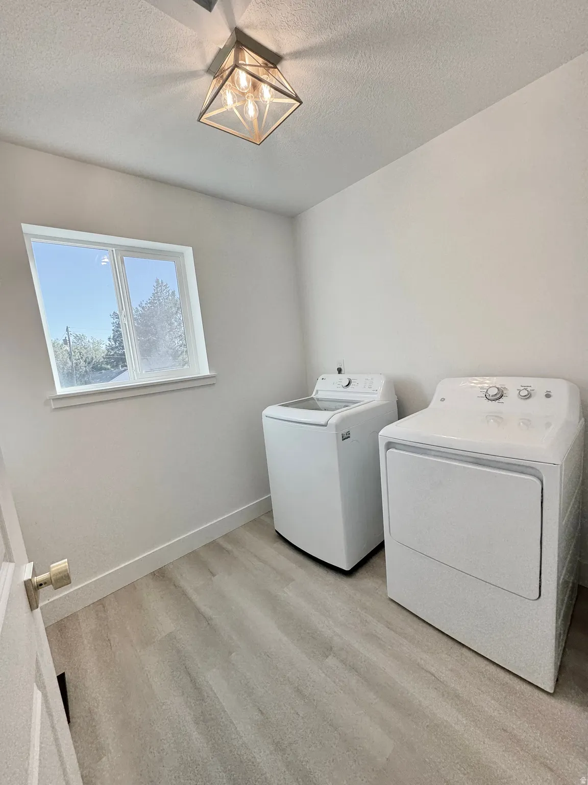 Laundry area featuring wood-finish flooring, a contemporary ceiling light fixture, and a window