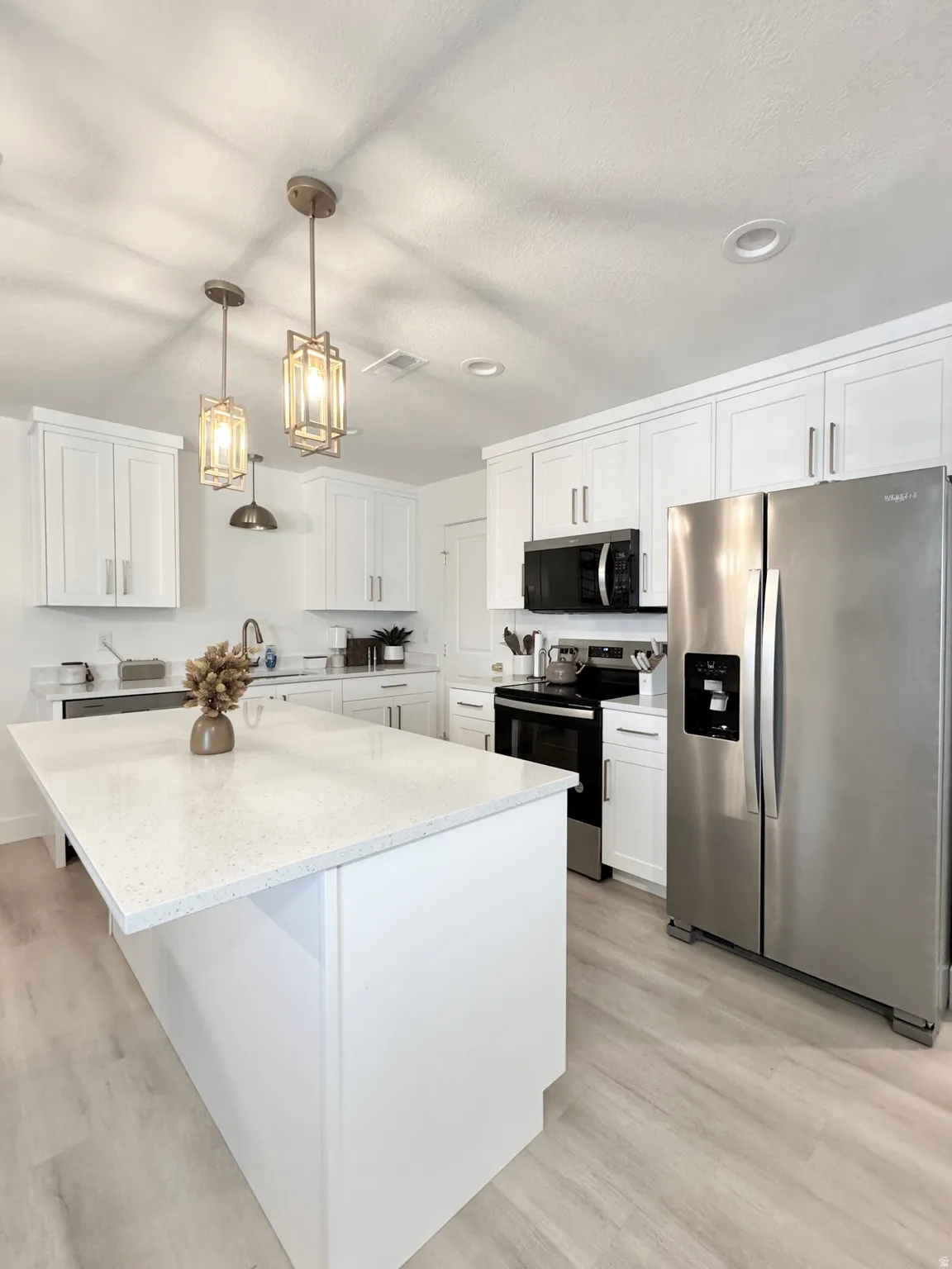 Modern kitchen featuring white shaker cabinetry, stainless steel appliances, and a large waterfall-edge island with white quartz countertops