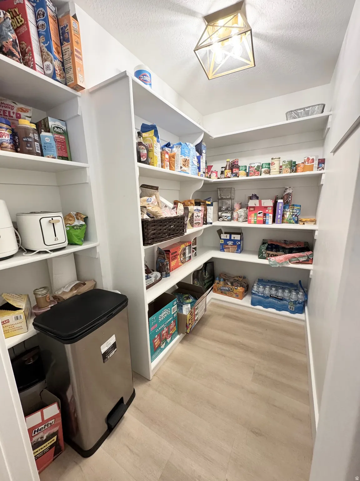 Spacious pantry featuring multiple built-in white shelving units, wood-finish flooring, and a decorative ceiling light fixture