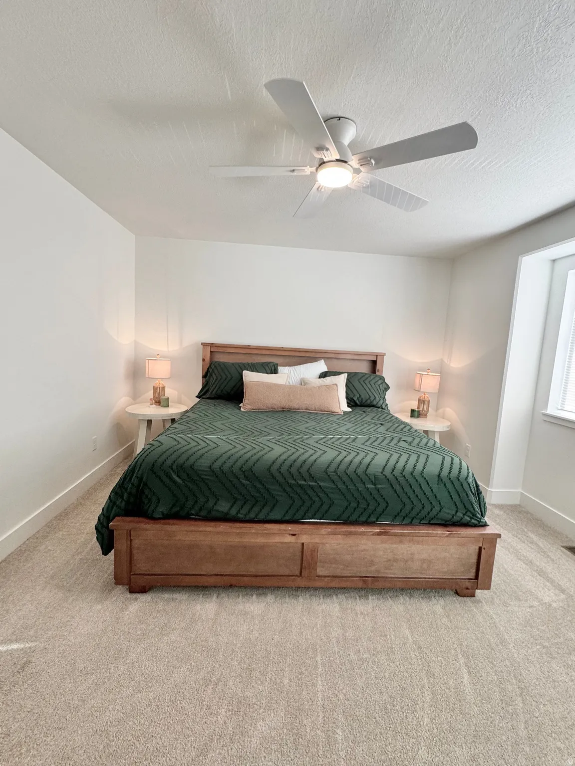Neutral tone carpet flooring, white painted walls, ceiling fan with integrated lighting, and a window with white trim