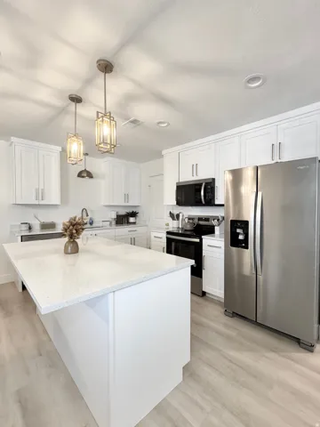 Modern kitchen featuring white shaker cabinetry, stainless steel appliances, and a large waterfall-edge island with white quartz countertops