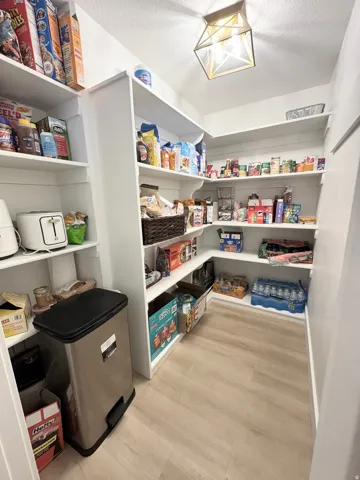 Spacious pantry featuring multiple built-in white shelving units, wood-finish flooring, and a decorative ceiling light fixture