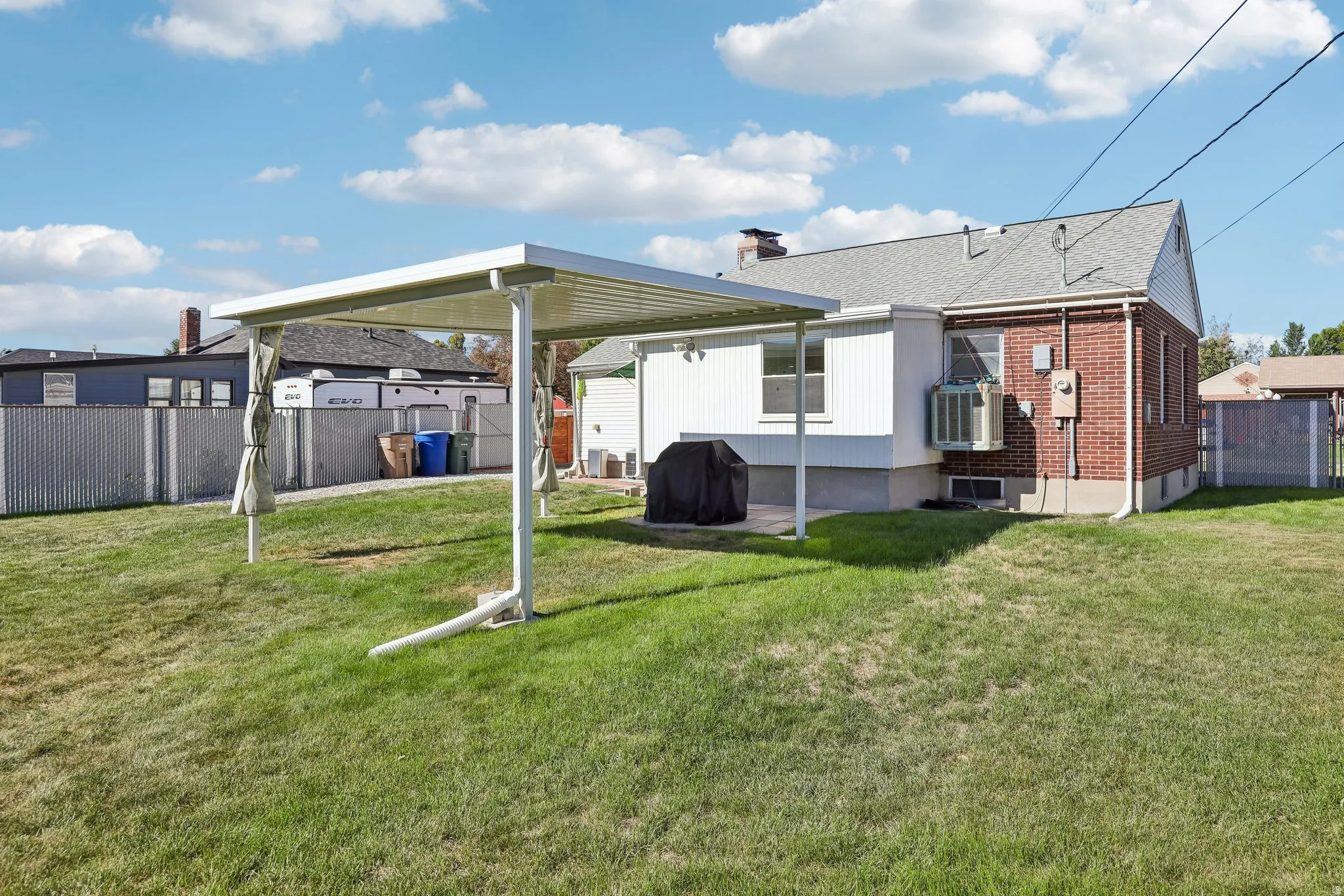 Expansive backyard featuring a white metal carport, brick and siding exterior, and chain-link fencing