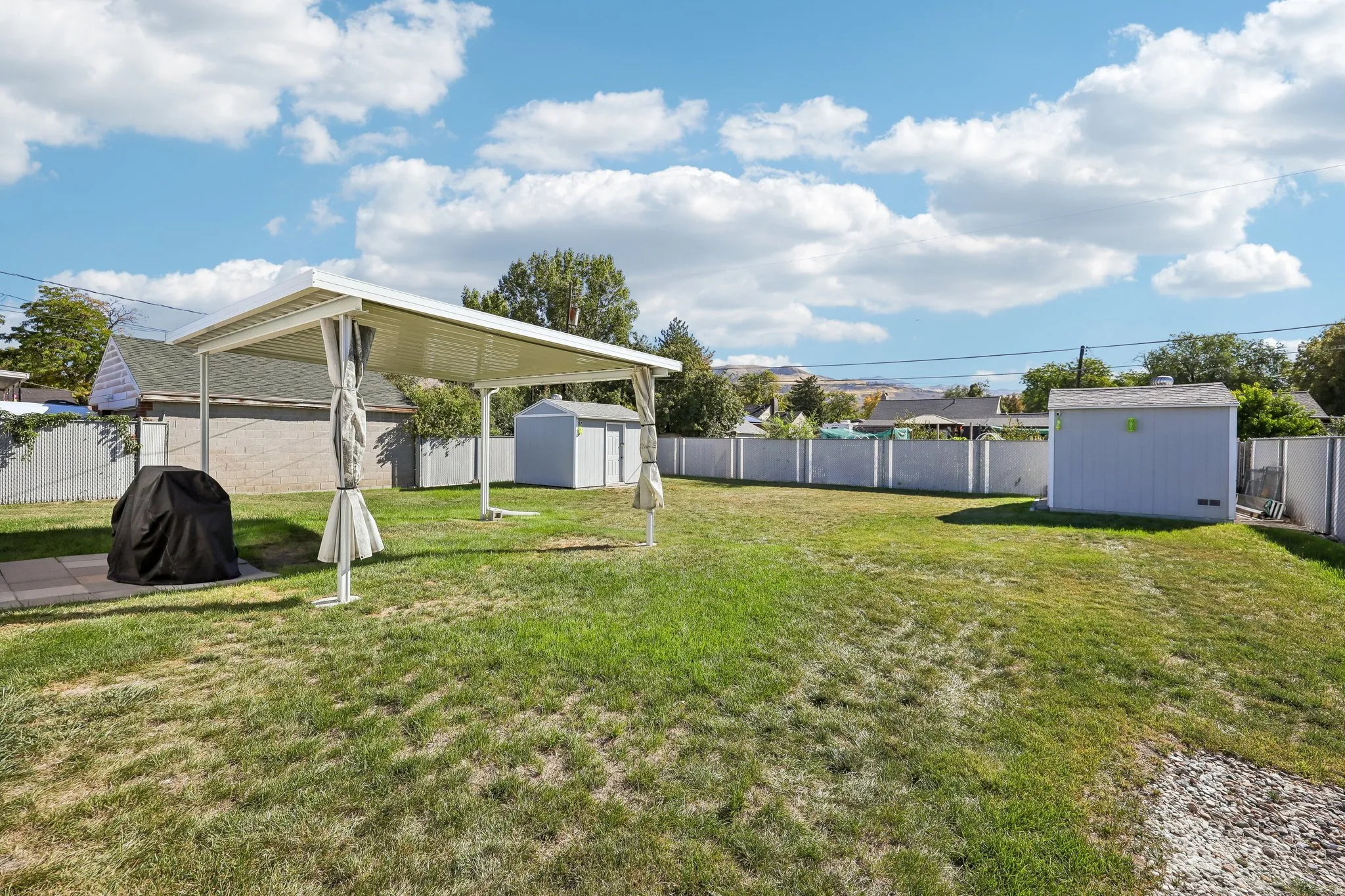 Expansive lawn area featuring a freestanding metal patio cover, a light-colored storage shed, and a privacy fence