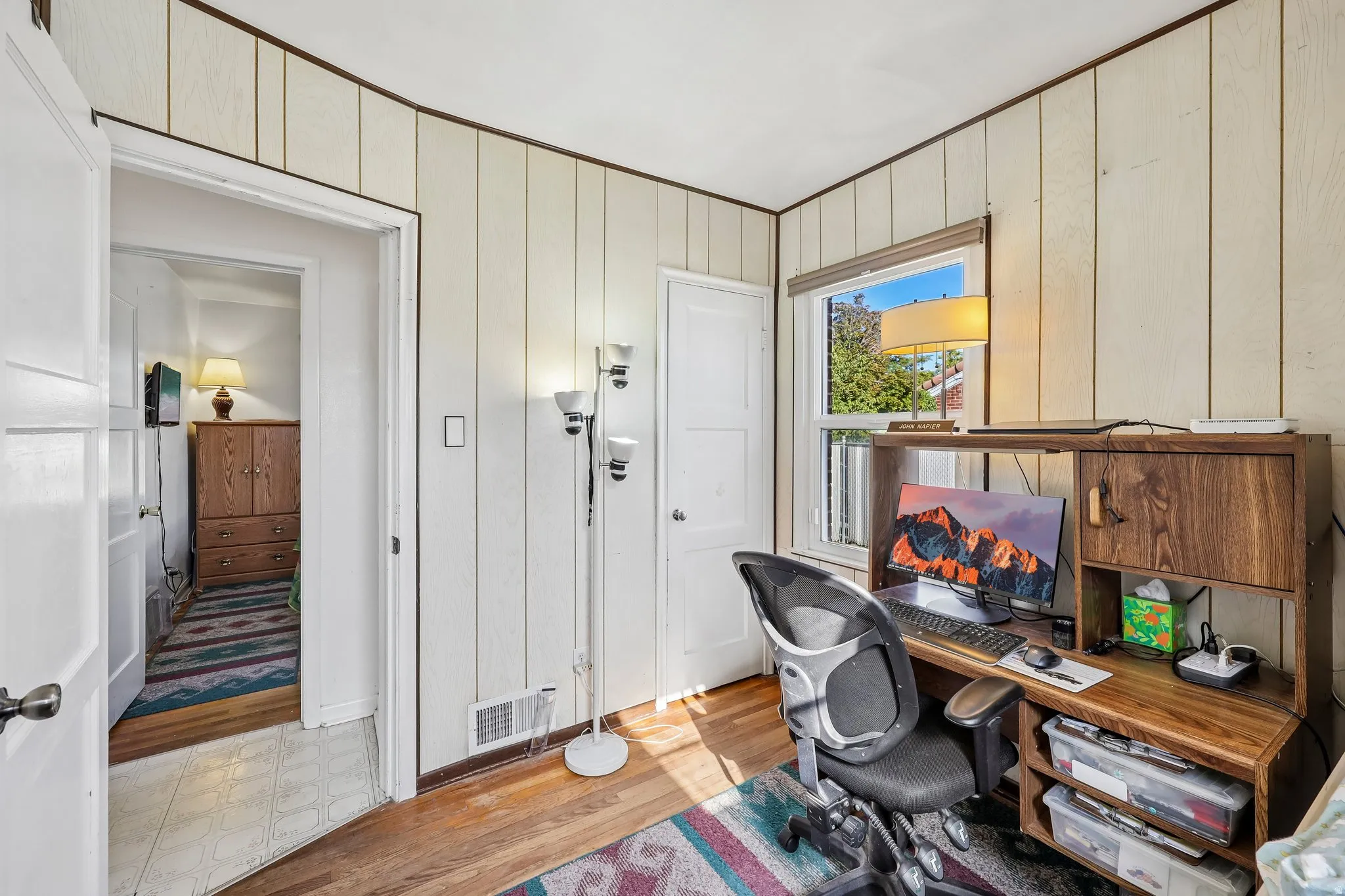 Wood-finish paneling, hardwood flooring, window with natural light, white painted doors, and a built-in wood-finish desk