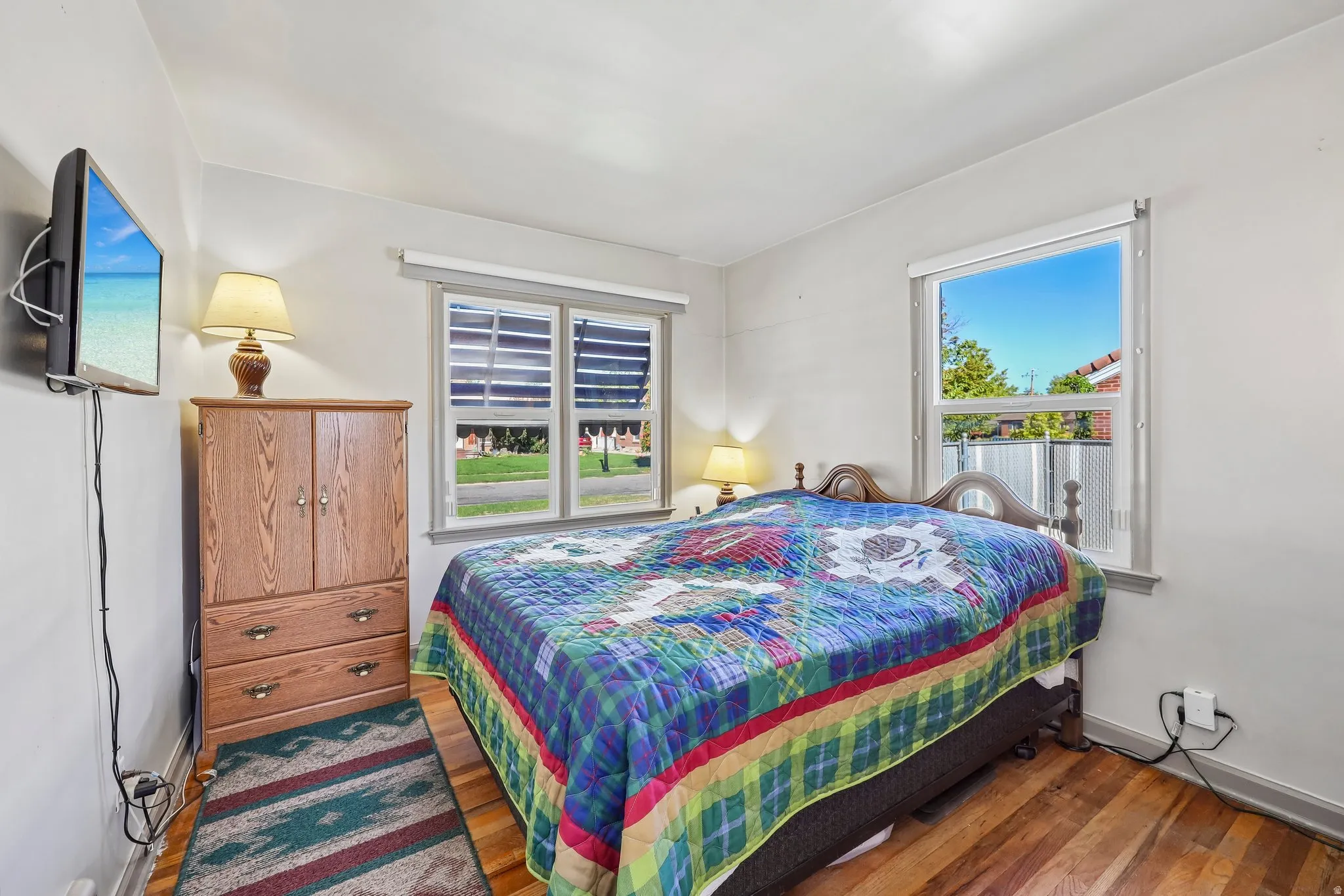 Hardwood flooring, twin windows with blinds, a wall-mounted television, and a built-in closet with drawers