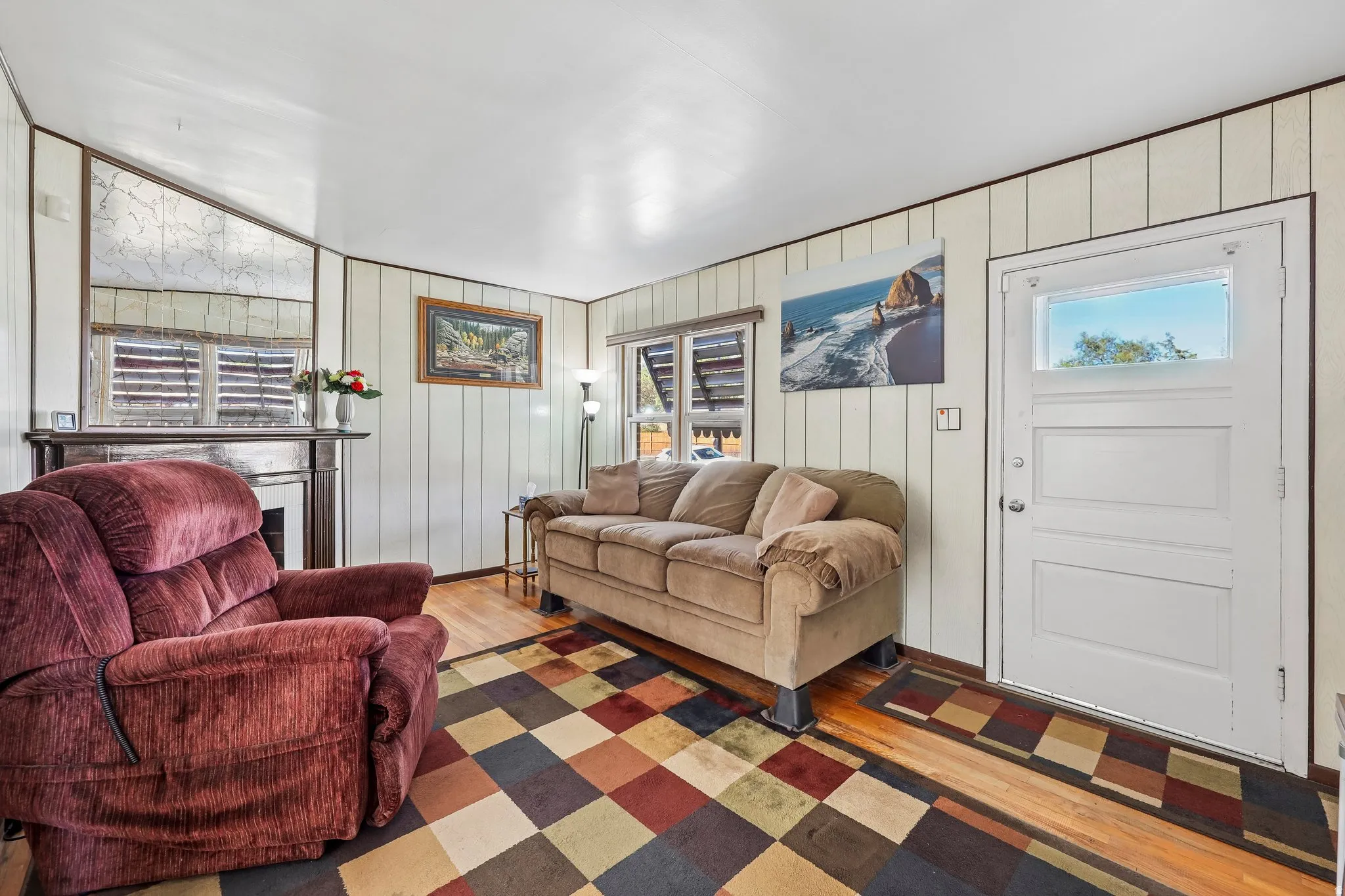Wood-finish flooring with vertical paneling, a classic fireplace with a decorative mantel, and a white entry door with an upper glass panel