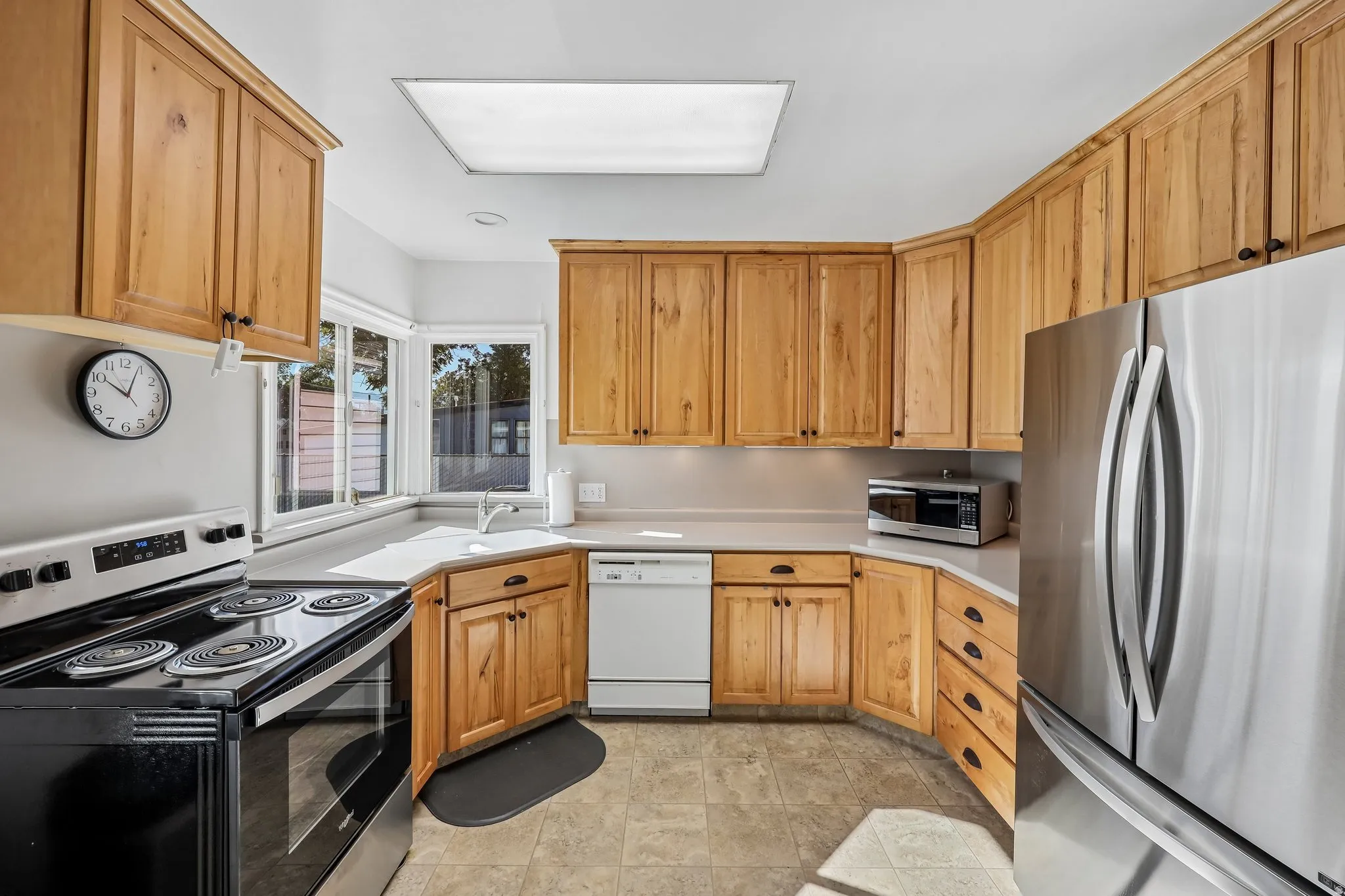 Kitchen featuring wood cabinetry, stainless steel refrigerator, white dishwasher, black electric range, and laminate countertops