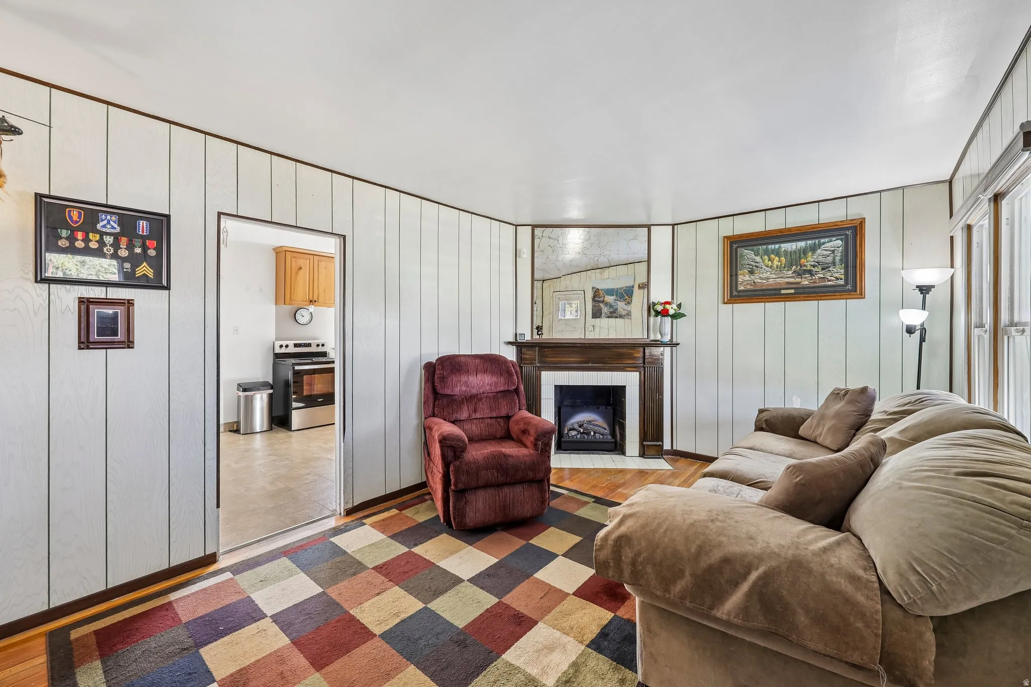 Living area featuring wood-finish flooring, vertical paneling, and an electric fireplace with a wood mantle