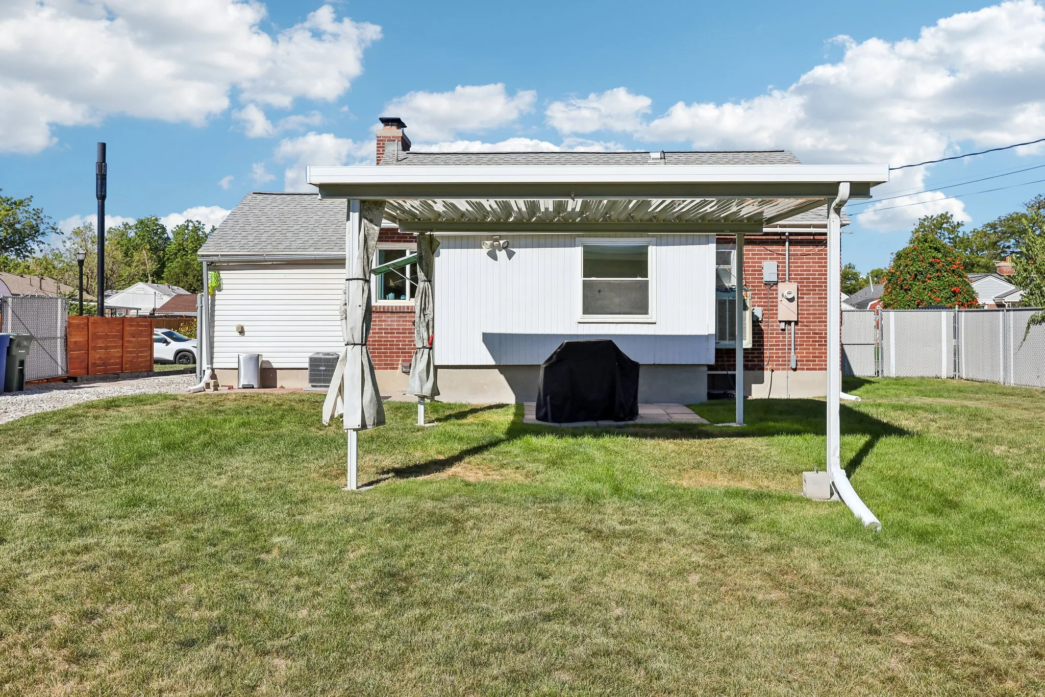 Expansive backyard featuring a lawn, a white pergola with a lattice roof, and a paved patio area