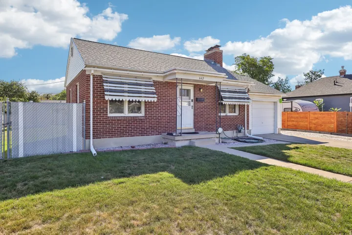 Brick exterior with a gabled roofline, attached garage, concrete driveway, and front sidewalk
