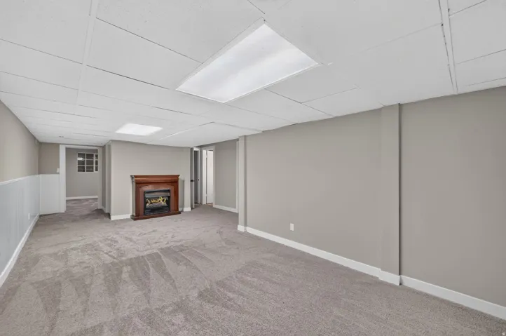 Spacious room featuring neutral carpeting, a wood-finish fireplace, and paneling accents