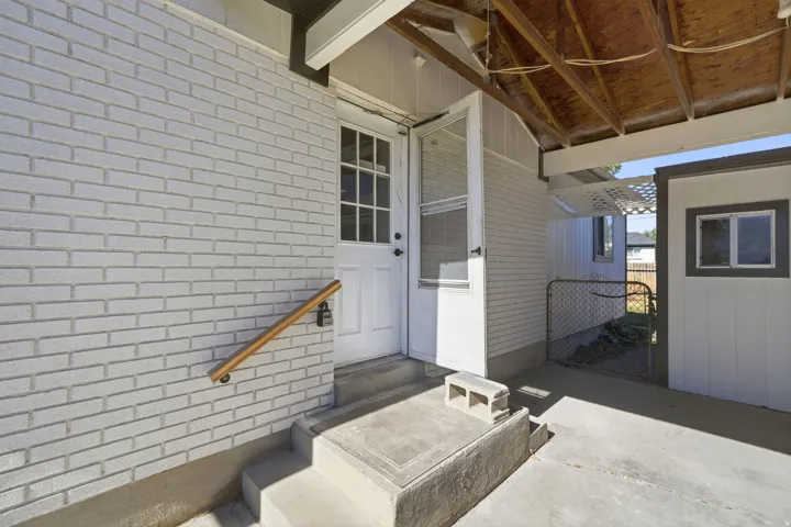 White brick exterior with a wood handrail, concrete steps, and a partially covered patio