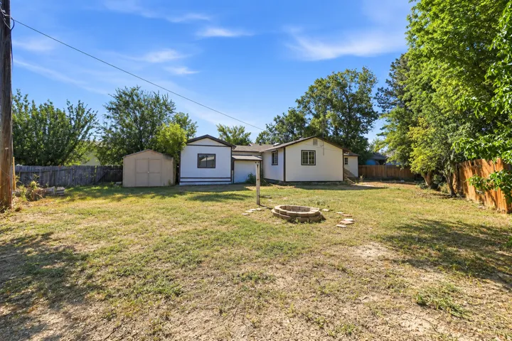 Expansive backyard featuring a stone-lined fire pit, perimeter fencing, and mature trees