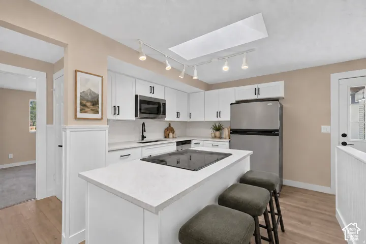 Kitchen featuring white cabinetry, light-toned countertops, stainless steel appliances, and a central island with an integrated cooktop
