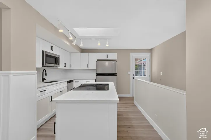 Modern kitchen featuring white cabinetry, stainless steel appliances, a center island with cooktop, and wood-finish flooring