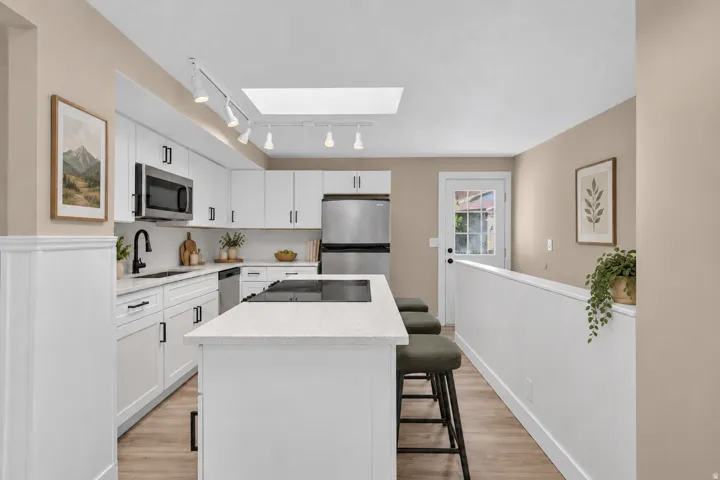 Kitchen featuring an island with built-in cooktop, stainless steel appliances, white cabinetry, a skylight, and wood-finish flooring