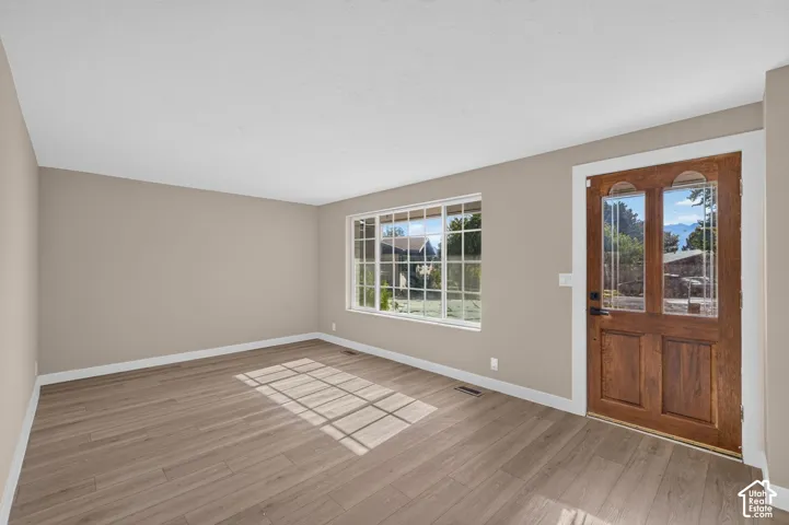 Wood-finish flooring, neutral wall tones, white trim, a multi-pane window, and a wood entry door with decorative glass