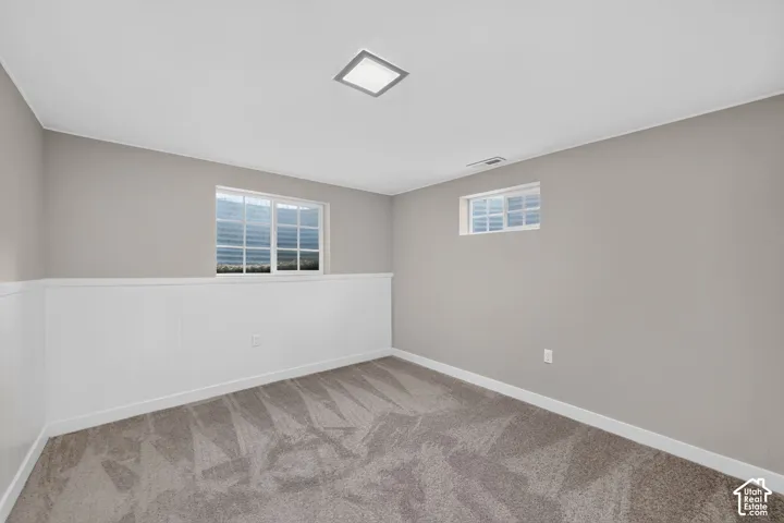 Neutral wall paint, white wainscoting, plush carpet, recessed ceiling light, and multiple windows