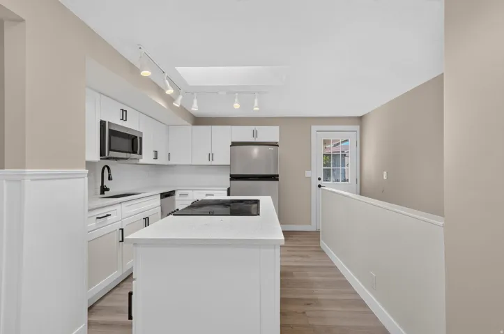 Modern kitchen featuring white cabinetry, stainless steel appliances, a center island with cooktop, and wood-finish flooring
