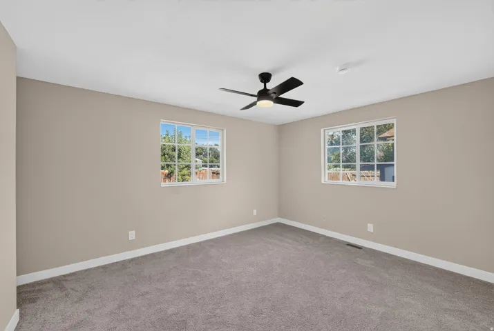 Carpeted flooring, neutral wall paint, two pane windows, and a ceiling fan with integrated lighting