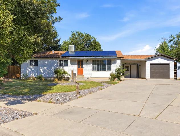 White brick exterior with solar panels, an attached garage, a concrete driveway, and a manicured lawn
