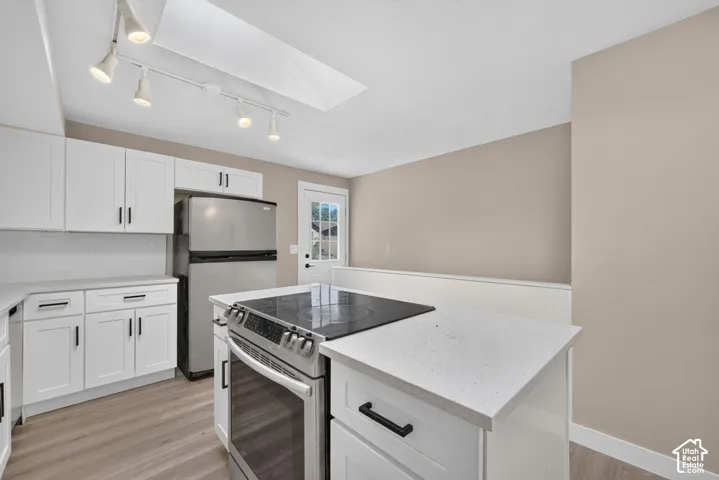 White shaker-style cabinetry with matte black hardware, light-toned countertops, stainless steel appliances, wood-finish flooring, and a skylight