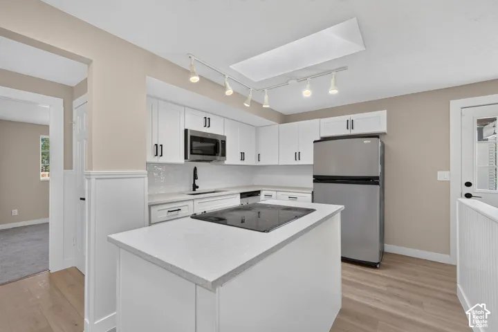 Kitchen featuring white cabinetry, light-colored countertops, stainless steel appliances, and wood-finish flooring