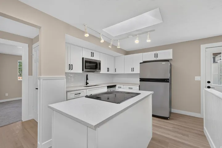 Kitchen featuring white cabinetry, light-colored countertops, stainless steel appliances, and wood-finish flooring