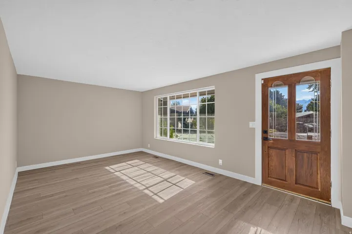 Wood-finish flooring, neutral wall tones, white trim, a multi-pane window, and a wood entry door with decorative glass
