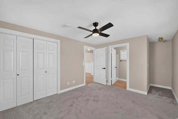 Ceiling fan with integrated lighting, neutral wall paint, white trim, paneled bifold closet doors, and carpet flooring