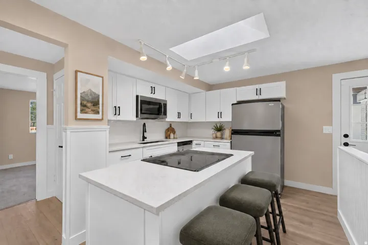 Kitchen featuring white cabinetry, light-toned countertops, stainless steel appliances, and a central island with an integrated cooktop